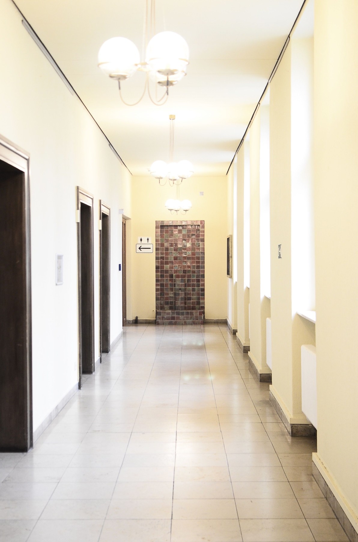 A bright hotel corridor with tiled flooring and visible grout lines.