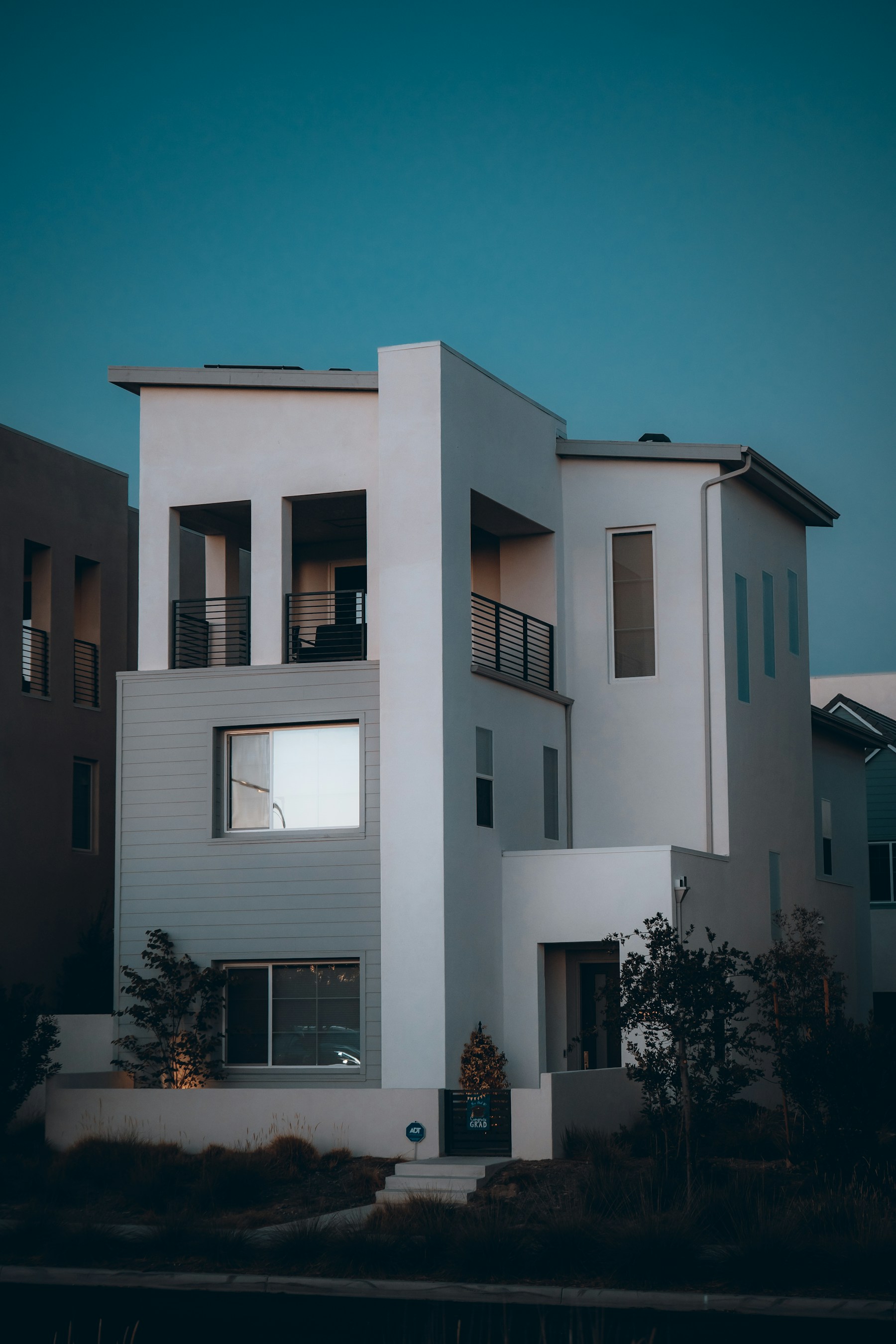 A contemporary stucco home photographed at dusk, with balconies and warm window light.
