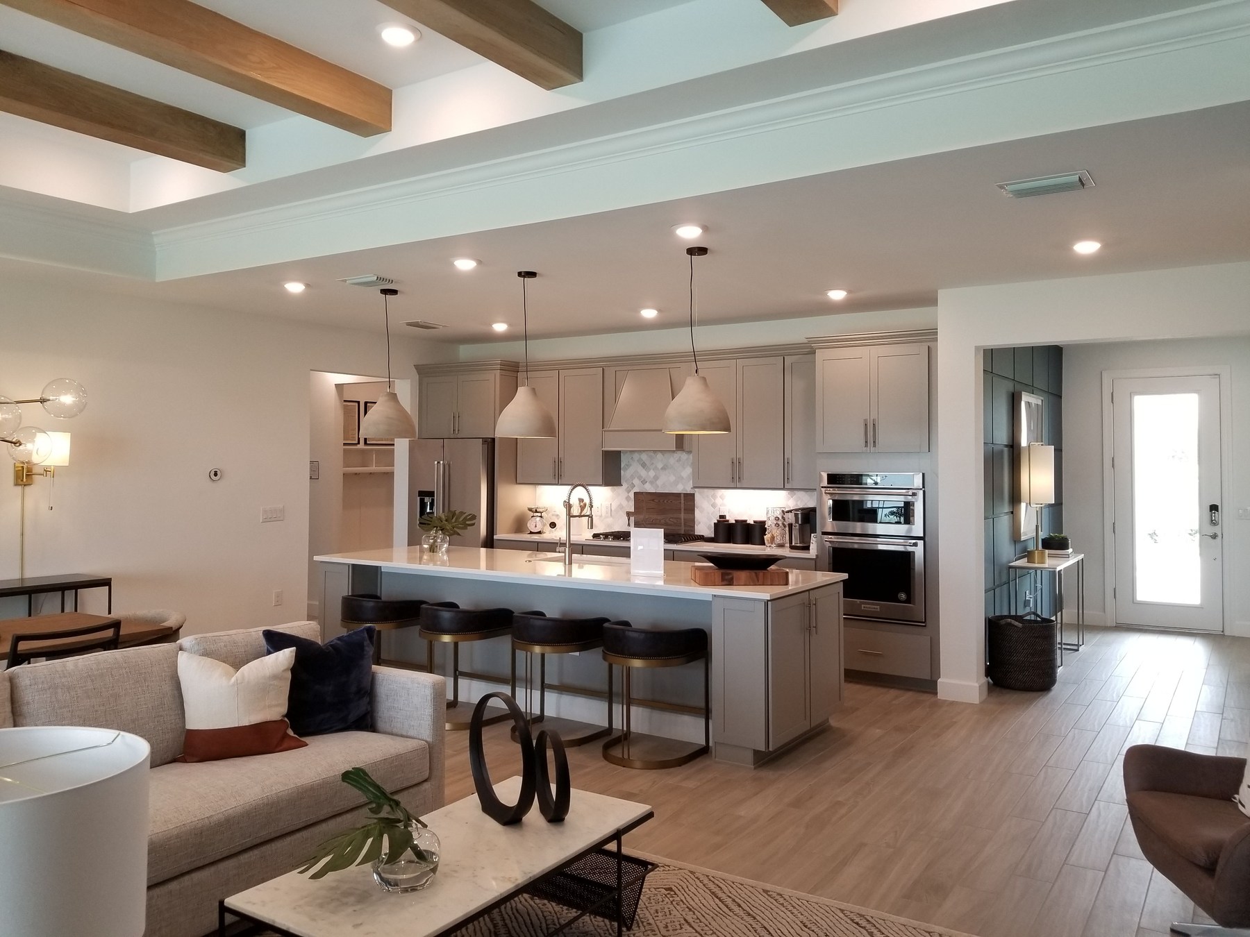 A furnished living room beside a contemporary kitchen with warm wood accents.